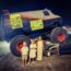 3 children stood in front of a monster truck at a car show